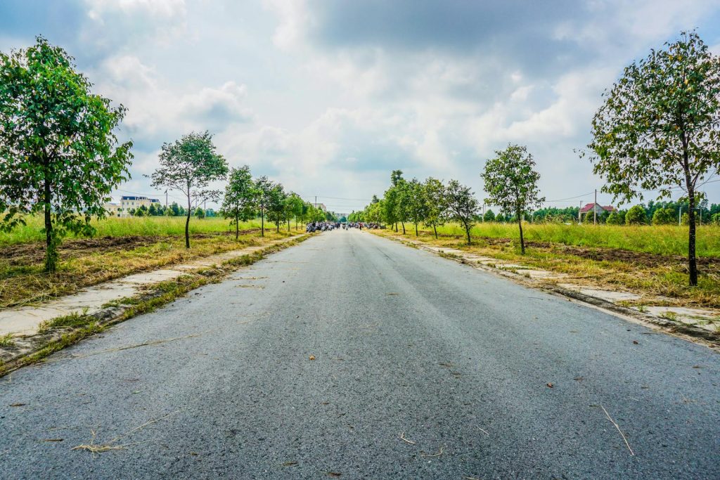A tranquil rural road under a cloudy sky with trees and fields lined along the way.