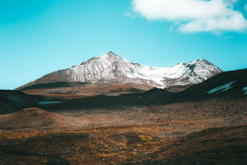 Stunning view of a snow-capped mountain range under a clear blue sky with rocky, earthy terrain.