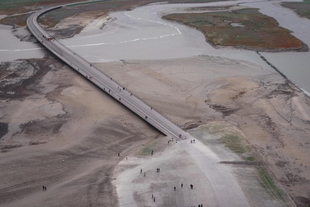 Aerial shot showing a bridge crossing over a barren landscape, sparse vegetation.