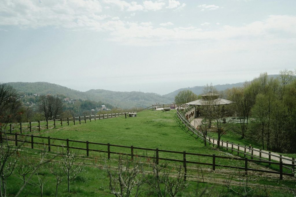 Beautiful rural landscape with green fields, hills, and a wooden fence under a clear sky.