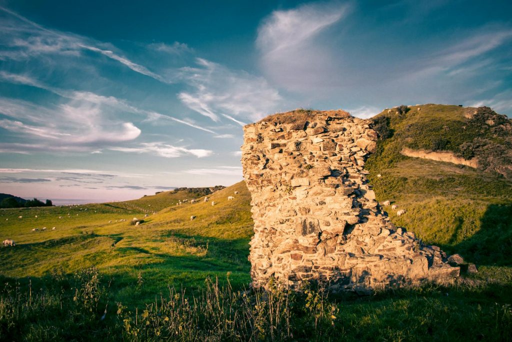 Scenic view of ancient stone ruins amidst lush green hills under a blue sky.