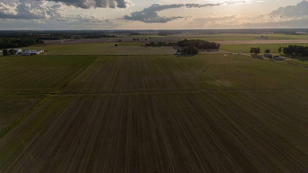 Drone shot of vast farmland with crop rows under a dramatic sunset sky.