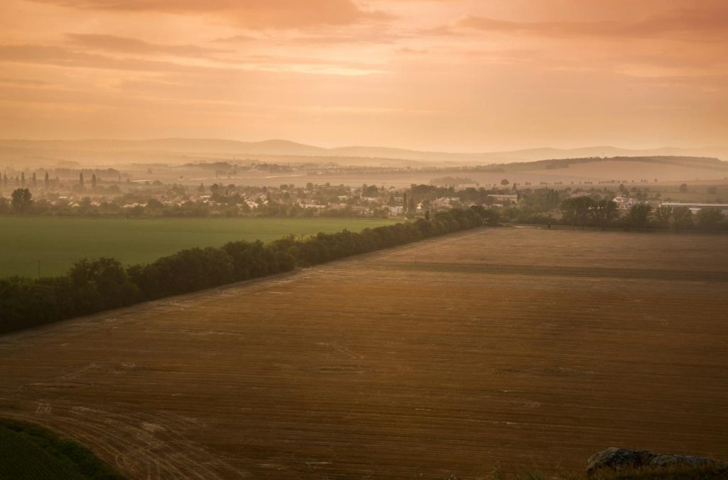 Aerial view of a picturesque countryside with fields and distant hills under a warm dawn sky.
