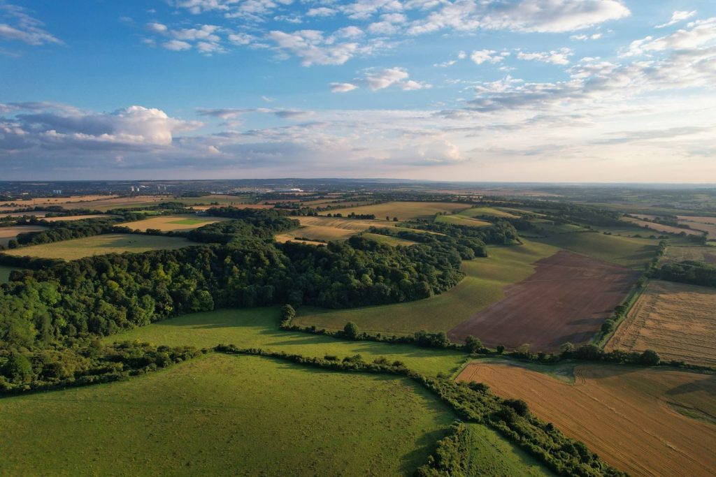 Scenic aerial view of Sharpenhoe's lush fields and woodlands under blue skies.