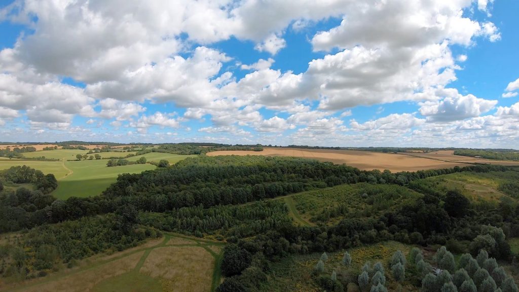 Panoramic aerial view of lush green fields and forests under a clear blue sky.