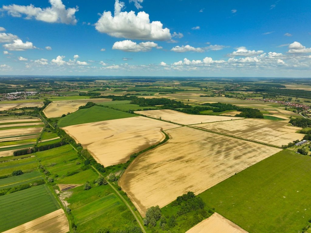 Aerial photograph of lush farmland under a bright blue sky in Garešnica, Croatia. Vibrant summer colors.